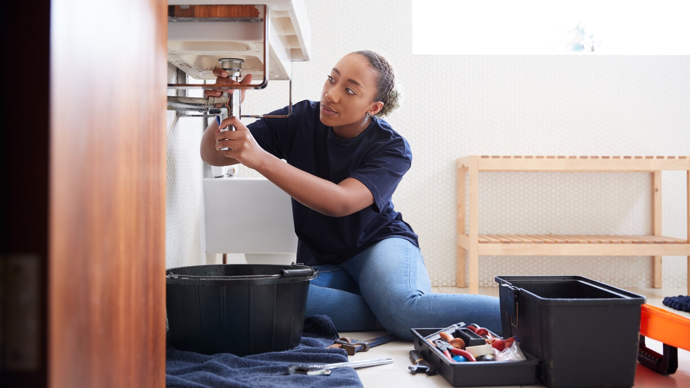 A woman with her toolbox fixing her sink drain.