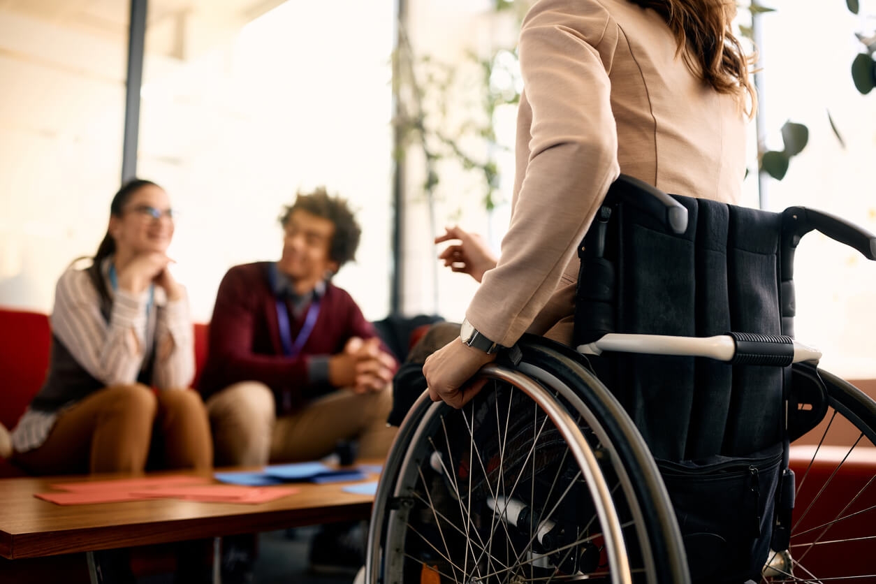 A woman in a wheelchair talking to her coworkers in an office.