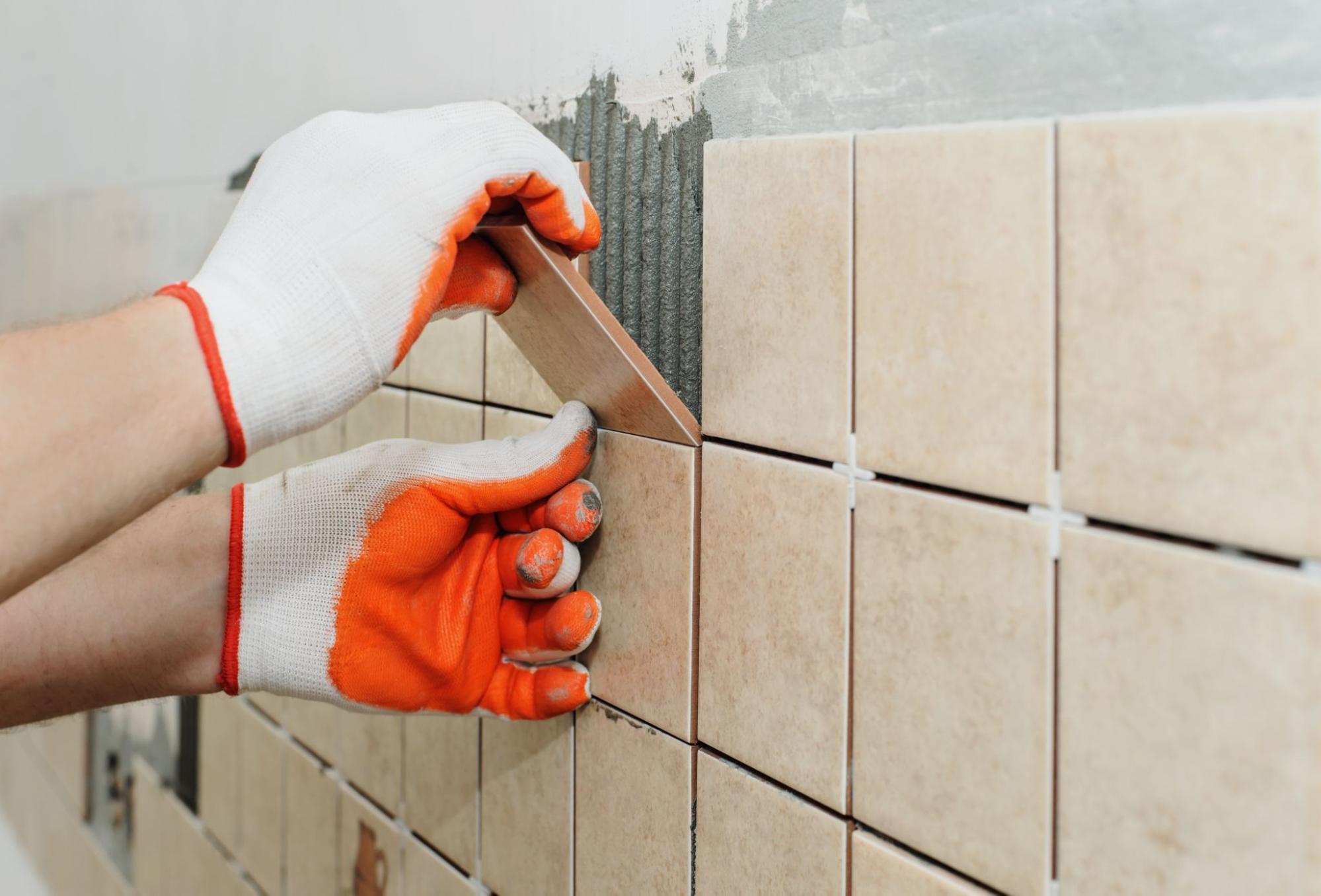 A person in orange and white gloves tiling a backsplash.